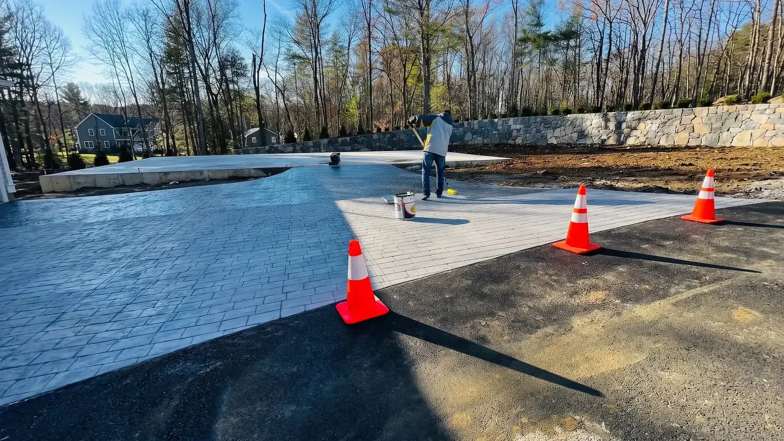 Worker applying sealant to a stamped concrete driveway before winter
